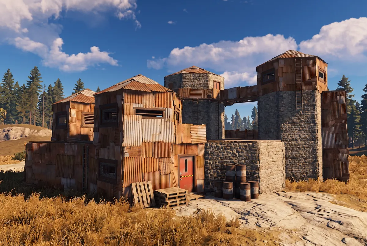 A multi-building Rust compound of patchwork sheet metal and grey stone in warm late-afternoon light.